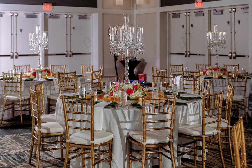 Ballroom with several tables, each topped with a lit crystal candelabra, and gold chiavari chairs throughout